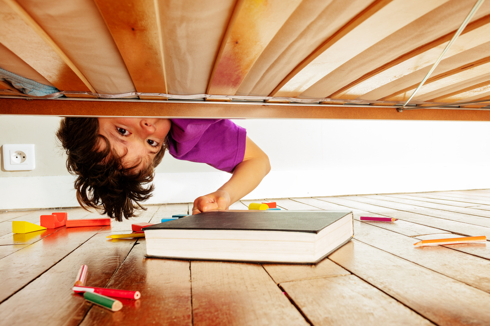 Child looking under bed to find lost book.