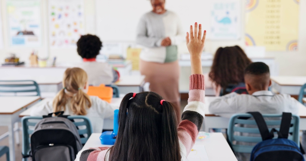 Single child raising hand in classroom to answer question.