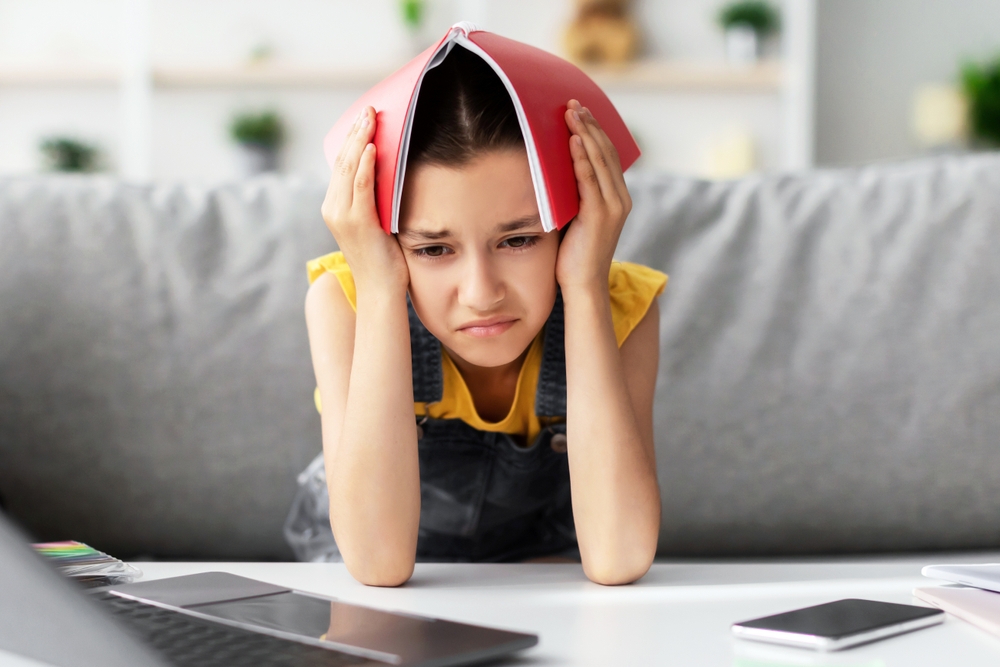 Child stressed out from school with binder over her head.