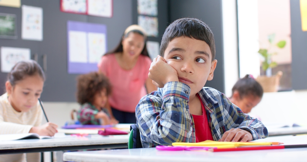 Child in class, looking away from school work bored and unfocused.